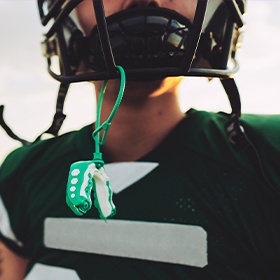 Football player with green mouthguard hanging from helmet